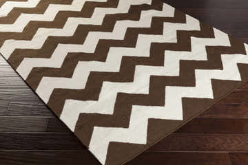 Close-up of the Soudan Area Rug, a hand-woven wool rug with a dark brown and ivory chevron pattern on dark wood floors. Corner