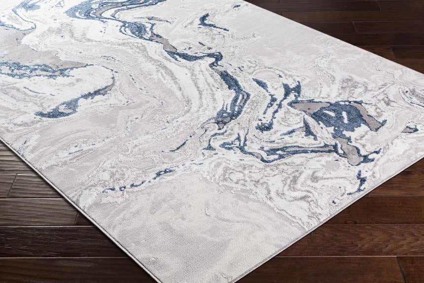 Close-up of the Speldhurst Blue Marble Rug. Features a cream base with dark blue, gray, and beige marble-like swirls. Corner