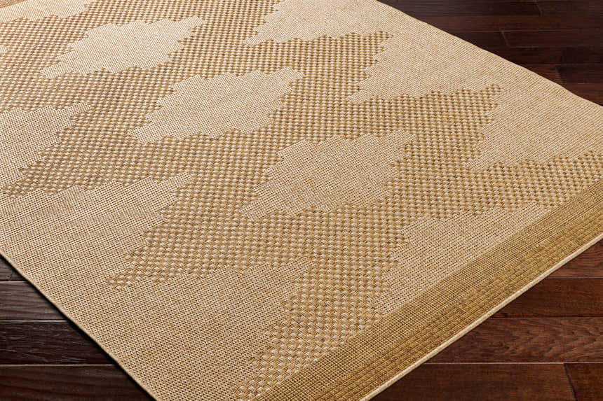 Close-up of a Colum Flatweave Faux Jute Rug. Tan and brown geometric pattern with a woven texture on dark wood flooring. Corner