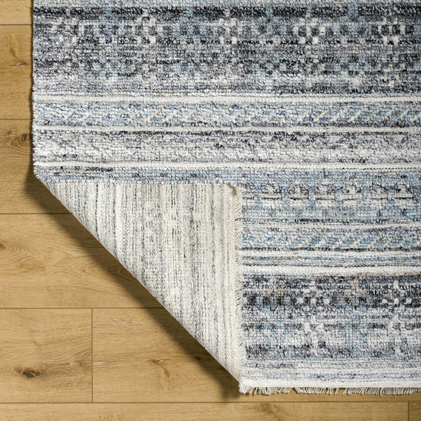Close-up of the Blue Adda Area Rug showing its Scandinavian design, blue, gray, and black colors, and hand-knotted texture. Fold