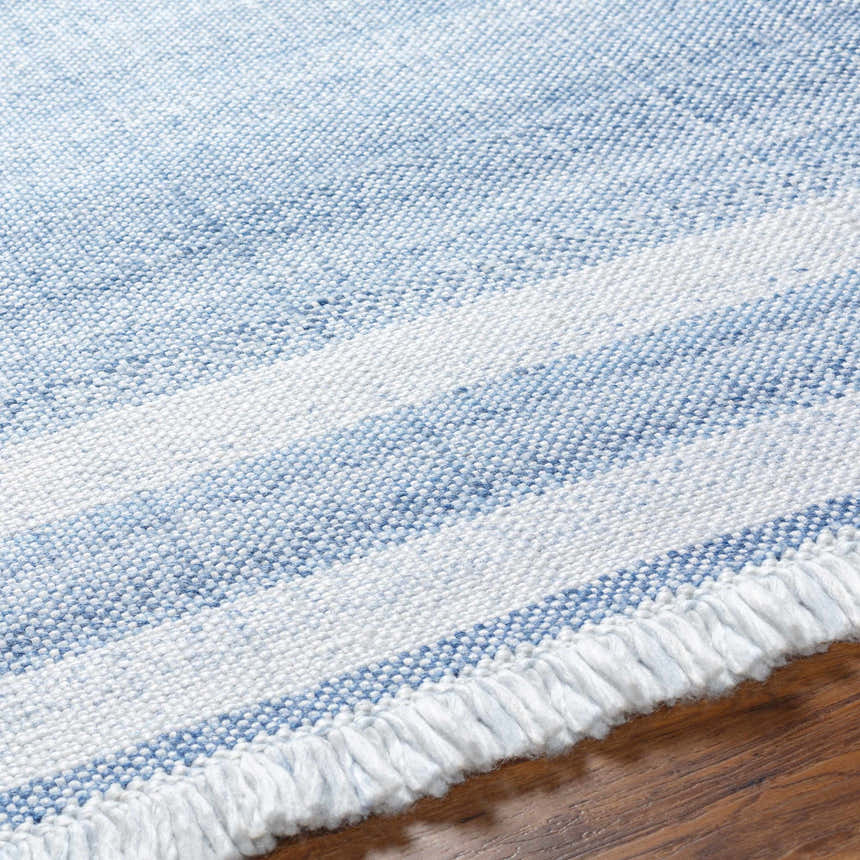 Close-up of the hand-woven Loic Silver Blue Area Rug, showing texture, blue and white stripes, and fringe detail. Texture