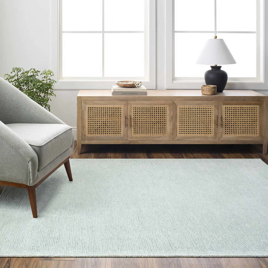 Living room scene with seafoam Isako washable rug, gray chair, wood cabinet, and natural light from windows. Roomscene-Rectangle
