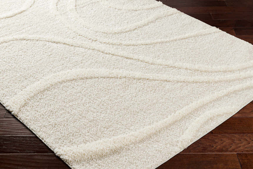 Close-up of the Horst Off White Area Rug, a shag rug with a subtle wave pattern, on dark wood flooring. Corner