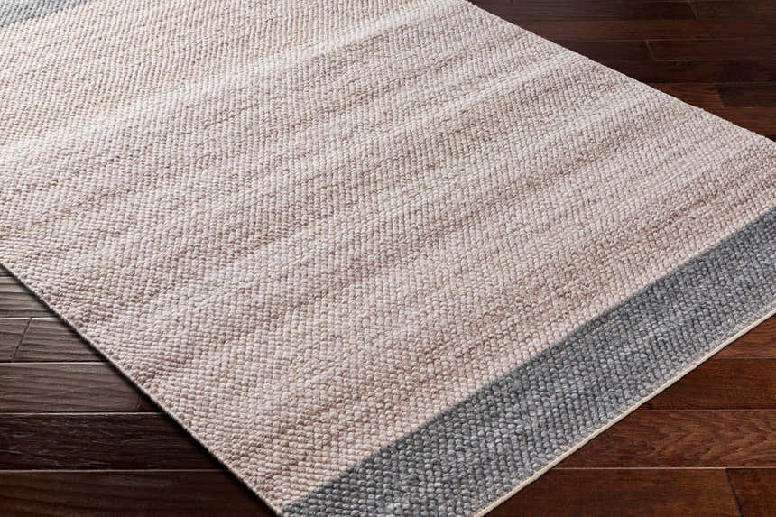 Close-up of the hand-woven Edwin Area Rug. Features a contemporary design in lambswool, brown, and gray recycled PET yarn. Corner