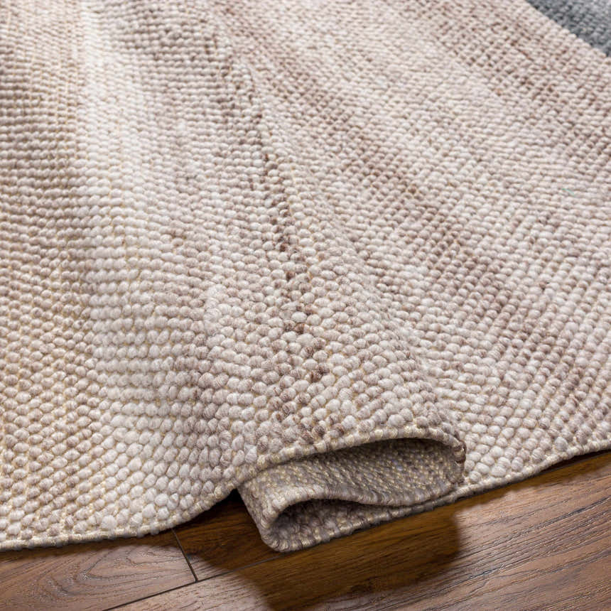 Close-up of the hand-woven Edwin Area Rug. The lambswool and brown rug has a textured, looped design on hardwood floors. Fold