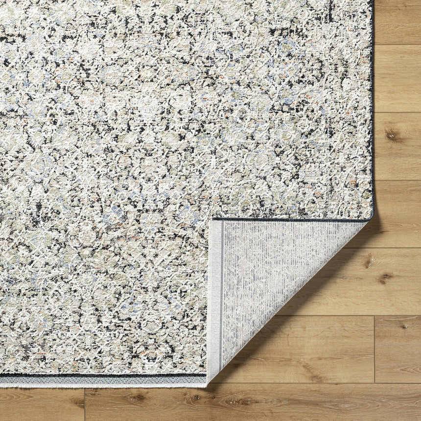 Close-up of the Haran Cloud Gray Area Rug showing its textured, abstract pattern and folded corner on a wood floor. Fold