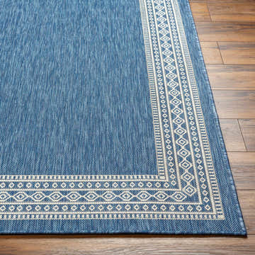 Close-up of the blue Aleli Blue Area Rug on wood floor, featuring a geometric border pattern. Front