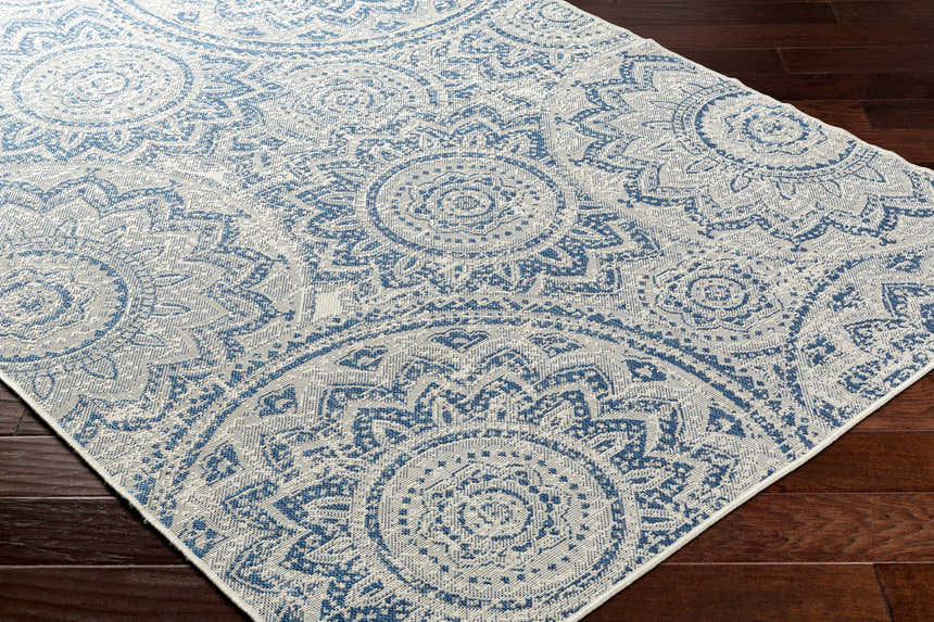 Close-up of the Ayala Blue Durable Rug featuring a traditional blue and ivory medallion pattern on dark wood floors. Corner