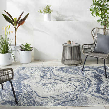 Outdoor patio scene with a Basma Blue Marble Area Rug, gray wicker chairs, a small table, and potted plants. Roomscene-Rectangle