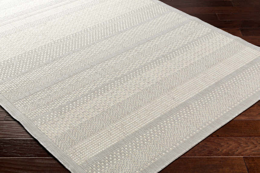 Close up of the Hessa Cream Area Rug showing its beige, gray, and bone woven texture on dark wood floors. Corner