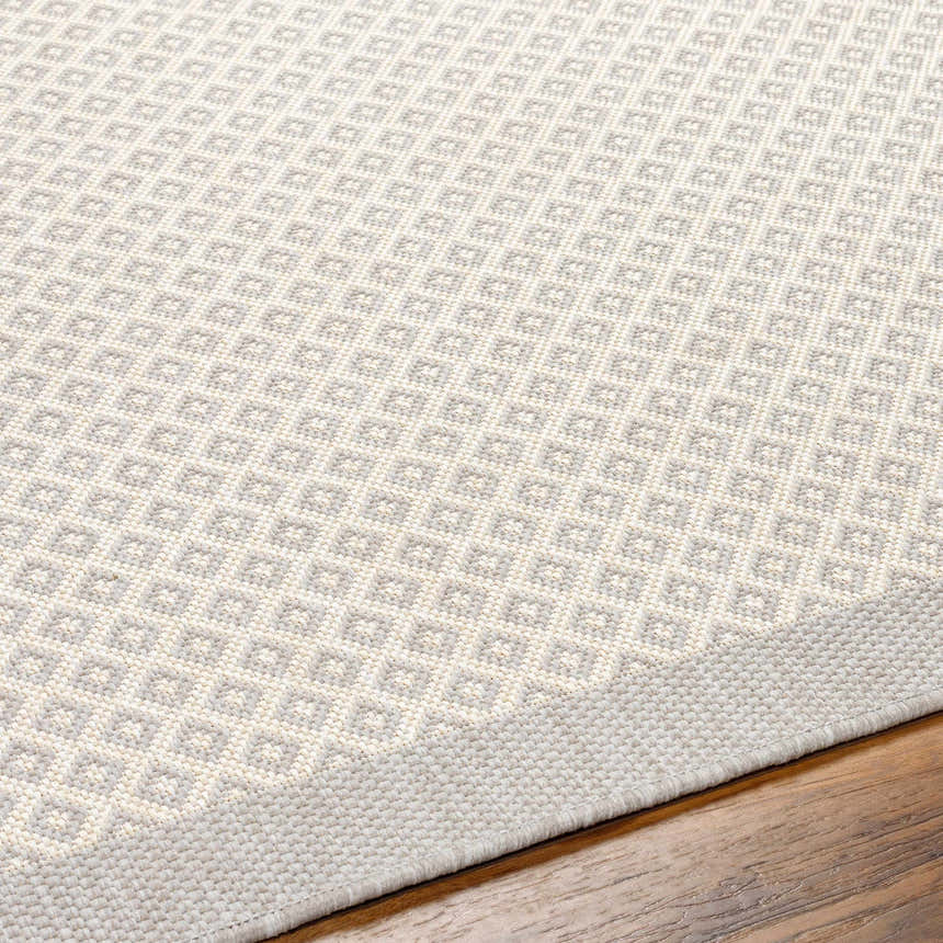 Close-up of the Suzu Area Rug showing a geometric diamond pattern in beige, bone, and gray on a wood floor. Texture