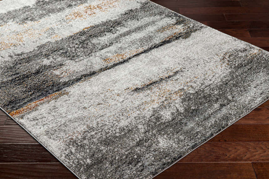 Close-up of Adam Gray Abstract Area Rug showing charcoal, gray, and brown tones on dark wood floor. Corner