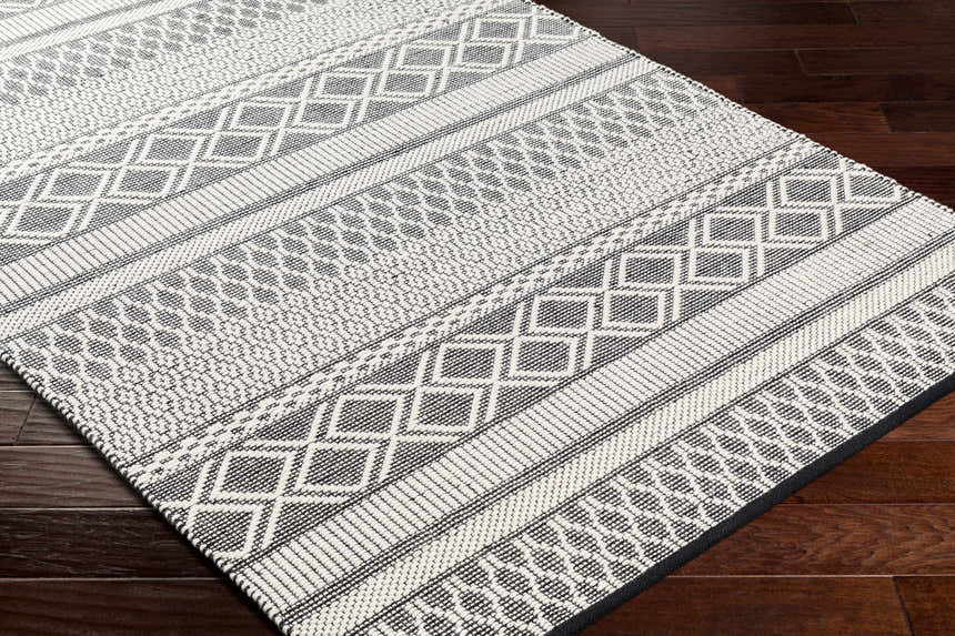 Close-up of the Hala Area Rug, a hand-woven wool rug with geometric patterns in dark gray, nickel, off-white, smoke, and taupe. Corner