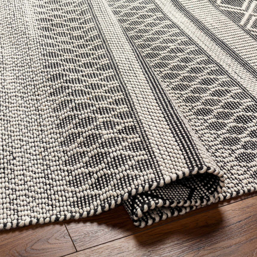 Close-up of Hala Area Rug, a hand-woven wool rug with geometric patterns in dark gray, nickel, off-white, smoke, and taupe. Fold
