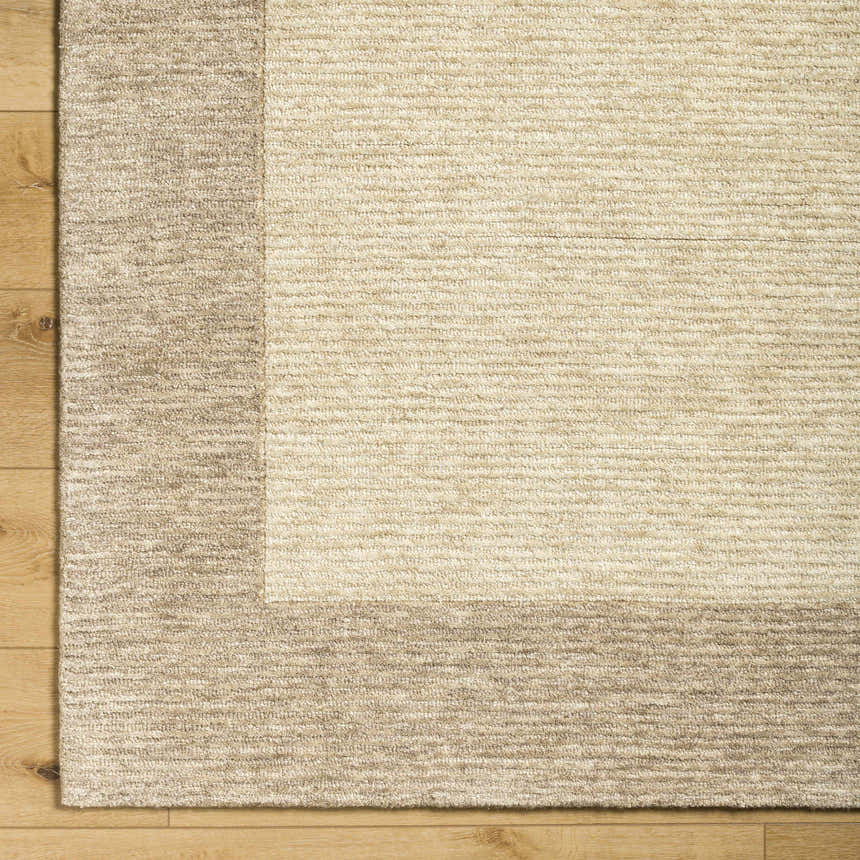 Close up of the hand tufted Amadi Area Rug. Wool rug in pearl and tan on wood floor. Corner