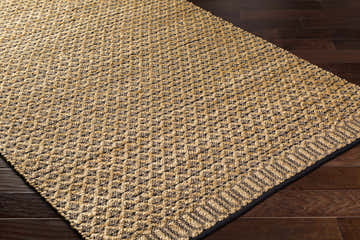 Close-up of hand woven Fruma Area Rug. Medium brown and nutmeg jute and cotton rug with a subtle geometric pattern. Corner