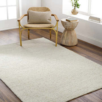 Scandinavian-style room with a cream Chaz Wool Rug, woven chair, and wood side table. Neutral tones create a calming mood. Roomscene-Rectangle