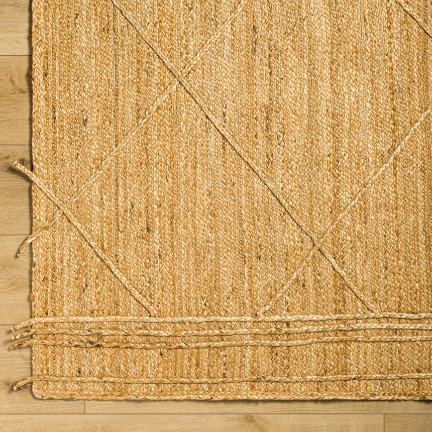 Close-up of hand woven Zeno Area Rug. Tan jute rug with braided detail and natural texture. Corner