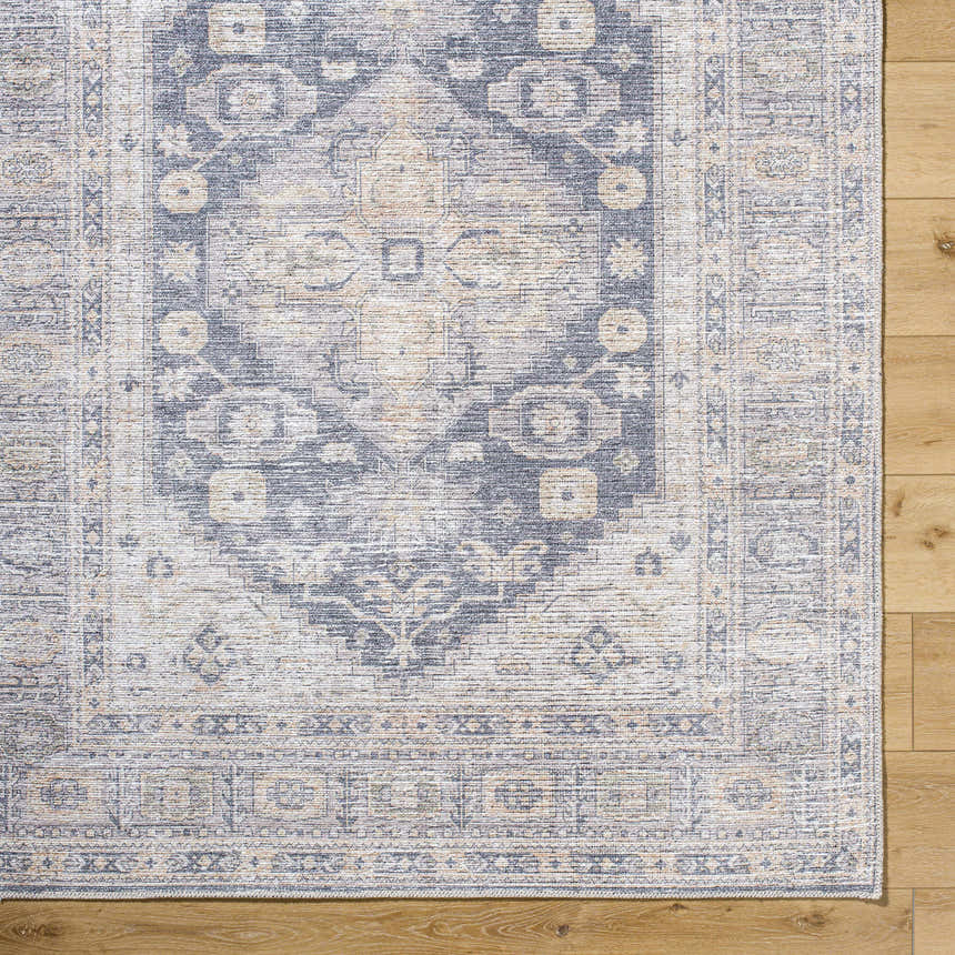 Close up of the corner of a Keola Washable Area Rug, showing a traditional pattern in gray, beige, and cream on wood floor. Corner