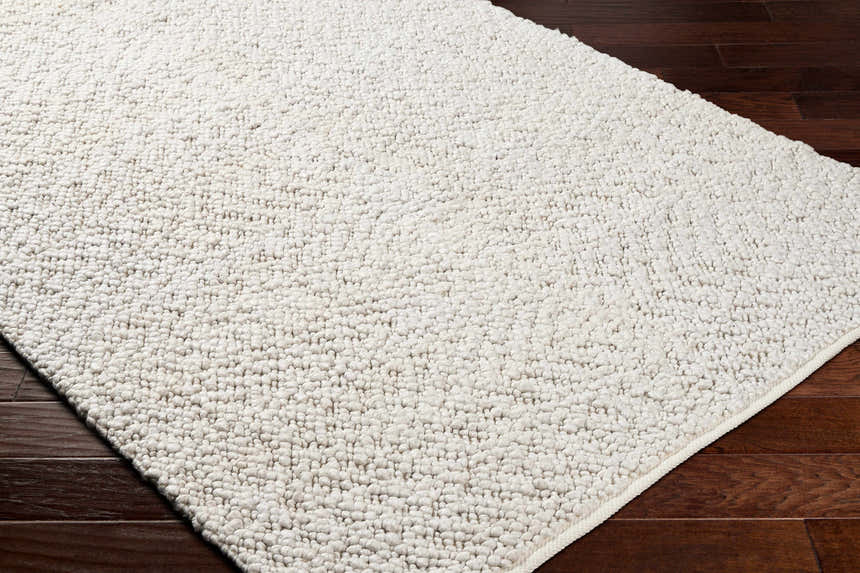 Close-up of the hand-woven Oved Area Rug in cloud gray, showing its textured, contemporary design on dark wood floors. Corner