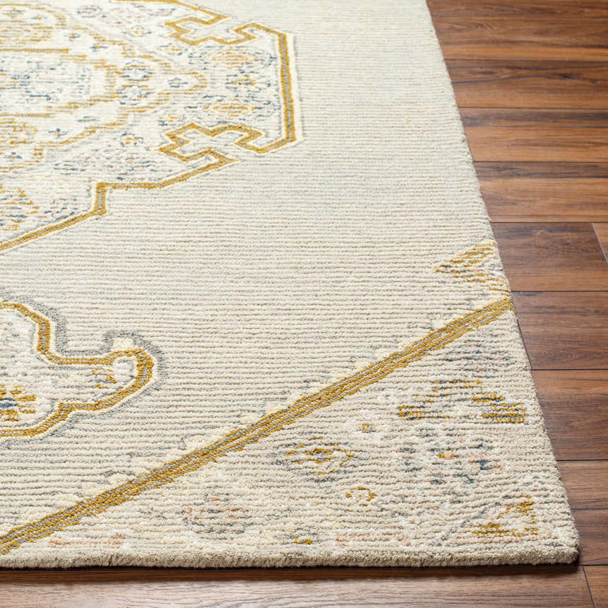 Close-up of the hand-tufted Mayu Area Rug. Beige wool rug with traditional gold and blue pattern on a wood floor. Front