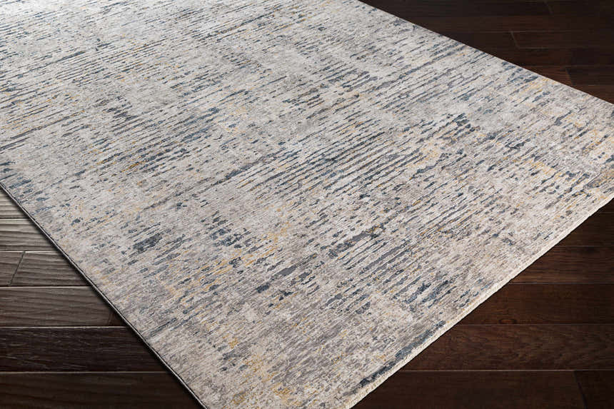 Close-up of Sywell Luxe Fringe Rug. Beige, blue, and charcoal abstract pattern on a soft polyester rug with fringe detail. Corner