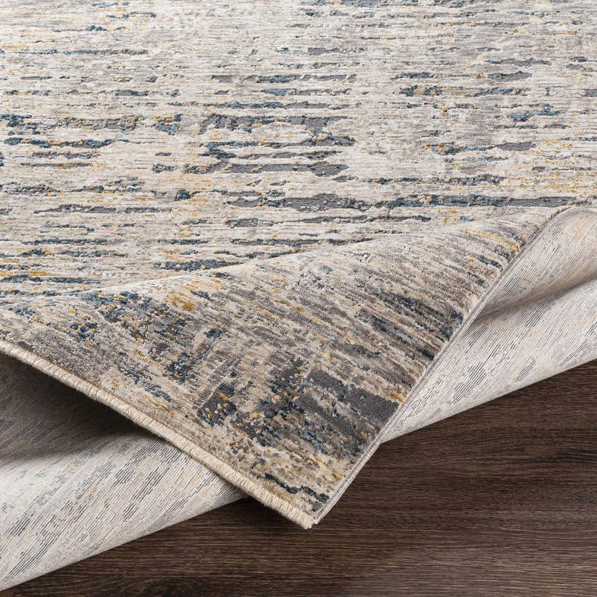 Close-up of the Sywell Luxe Fringe Rug showing its beige, blue, and charcoal contemporary pattern and soft polyester texture. Fold