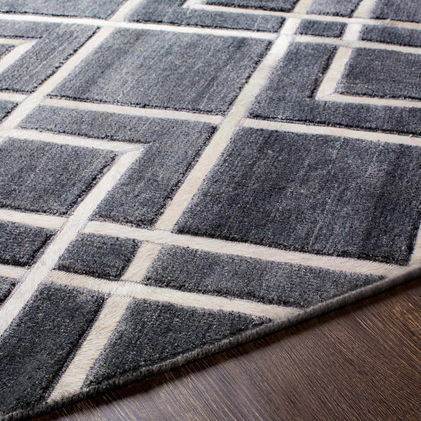 Close-up of the gray Taclobo Area Rug with a light gray geometric pattern on a dark wood floor. Texture