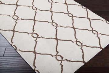 Close-up of the Tadley Area Rug. Beige wool rug with a brown geometric lattice pattern on dark wood floors. Corner