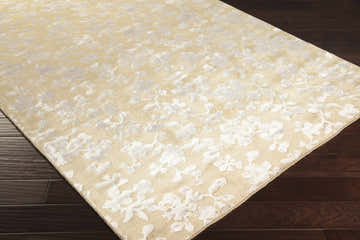 Close-up of the Talkeetna Area Carpet. Hand-knotted, contemporary style rug with a floral pattern in ivory and light gold tones. Corner