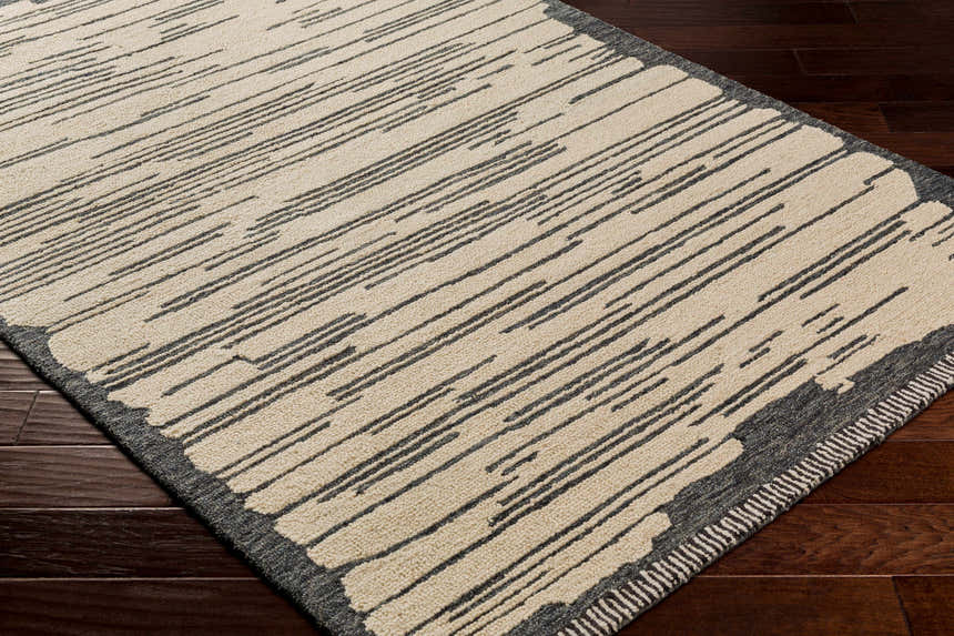 Close-up of the hand-tufted Tapas Wool Area Rug. Features a cream base with black, charcoal, and oatmeal striped pattern. Corner