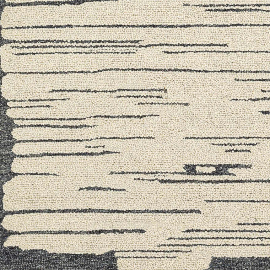 Close-up of the hand-tufted Tapas Wool Area Rug. Features a cream base with charcoal and black horizontal stripes. Swatch