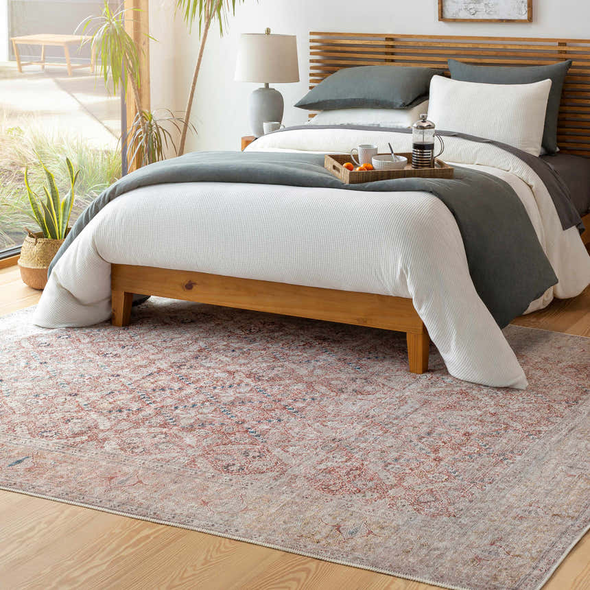 Bedroom scene with a Tapia Washable Area Rug in brick red, blue, and gray under a wooden bed with white and gray bedding. Roomscene-Rectangle