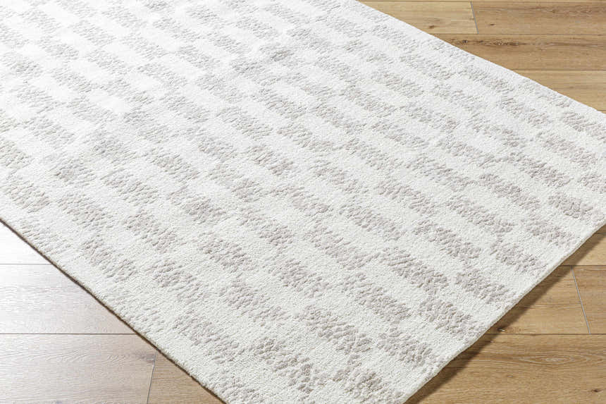 Close-up of the Theda Area Rug. Hand-tufted wool rug in ash, light silver, and off-white with a subtle geometric pattern. Corner