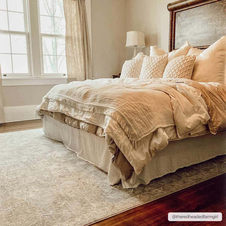 Bedroom scene with a beige Wurtulla Thick Luxe Statement Rug under a bed with layered bedding and neutral tones. Roomscene-Rectangle