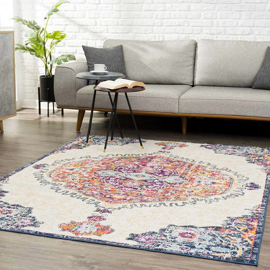 Living room scene with a Tigrit Blue & Orange area rug, gray sofa, side tables, and plant against a white brick wall. Roomscene-Rectangle