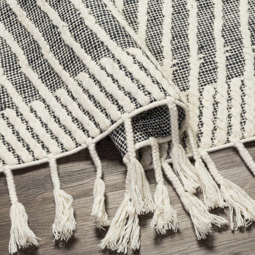 Close-up of the Tamayong Tasseled Jute & Wool Rug. Black and cream striped pattern with long, textured tassels. Fold