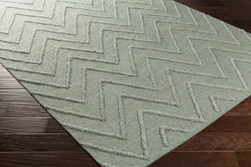 Close-up of the Trampas Clearance Jute Area Rug in pale blue with a textured, zig-zag pattern on a dark wood floor. Corner