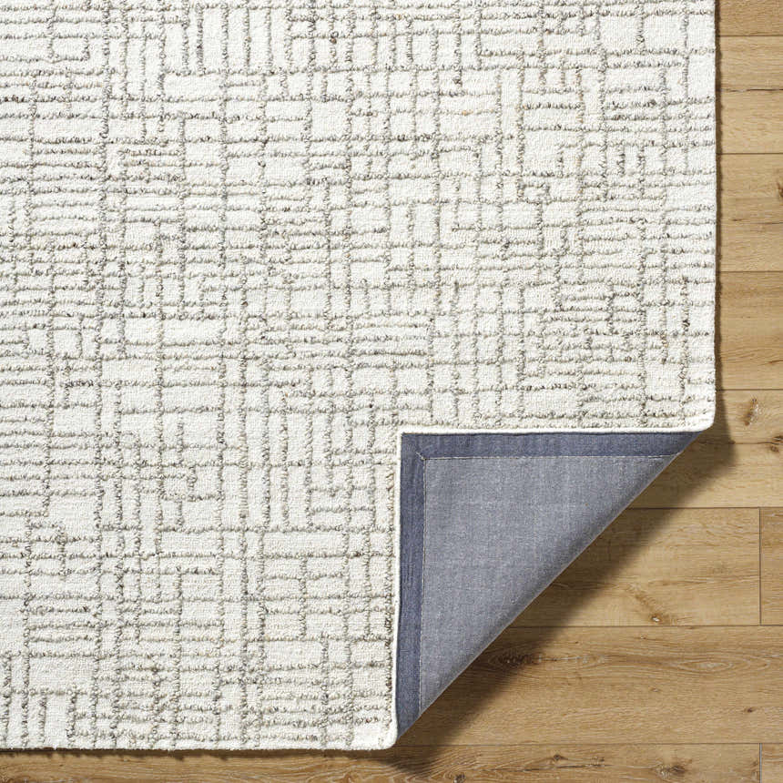 Close-up of the hand-tufted Tibby Area Rug. Light silver wool rug with a geometric grid pattern in silver gray on hardwood floor. Fold