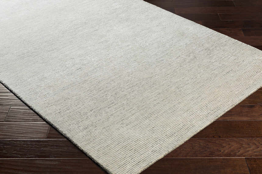 Close-up of the Orcas Hand Tufted Wool-Blend Rug - Aqua showing its cream color and subtle striped texture on dark wood floors. Corner