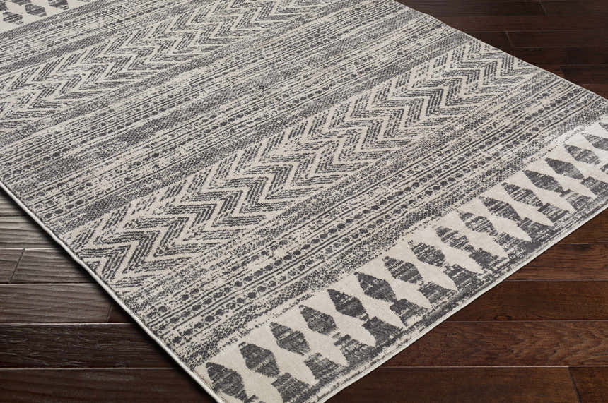 Close up of the Tuy Area Rug showing the dark gray bohemian-inspired geometric pattern and distressed texture. Corner