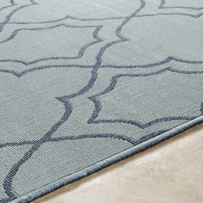 Close-up of the Ursa Area Rug. Pale blue olefin rug with a navy geometric trellis pattern and bound edge. Texture