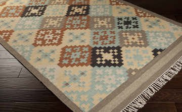Close-up of the hand woven Waddy Area Rug. Geometric pattern in beige, brown, sage, and gray. Wool rug with fringe. Corner