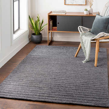 Living room scene with charcoal Warrendale Area Rug, wood floors, modern cabinet, and white chair. Roomscene-Rectangle