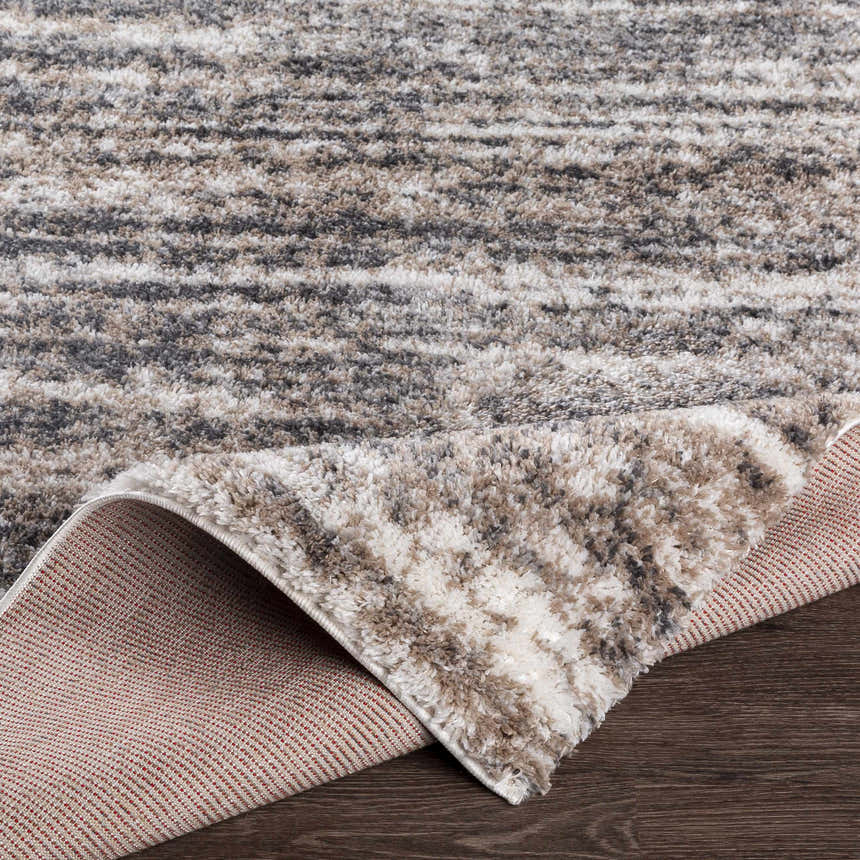 Close-up of the Weddin Striped Plush Area Rug. Charcoal, cream, gray, and tan stripes. Plush texture. Fold
