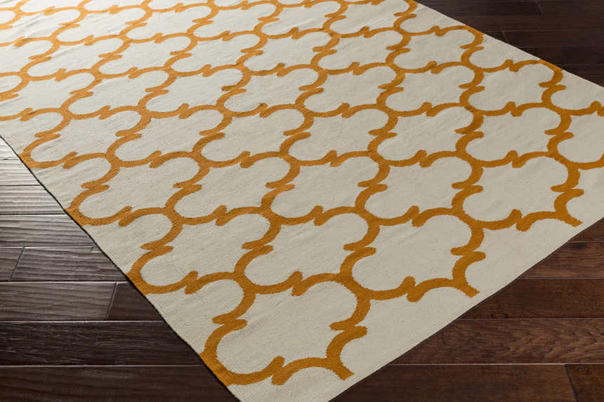 Close-up of the Weehawken Area Rug. Ivory rug with a bright orange quatrefoil pattern on dark wood floors. Corner
