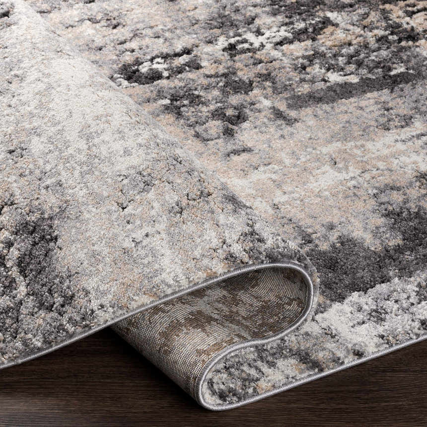 Close-up of the Witchford Abstract Charcoal Thick Rug showing its texture, colors (black, gray, ivory, tan) and machine-woven construction. Fold