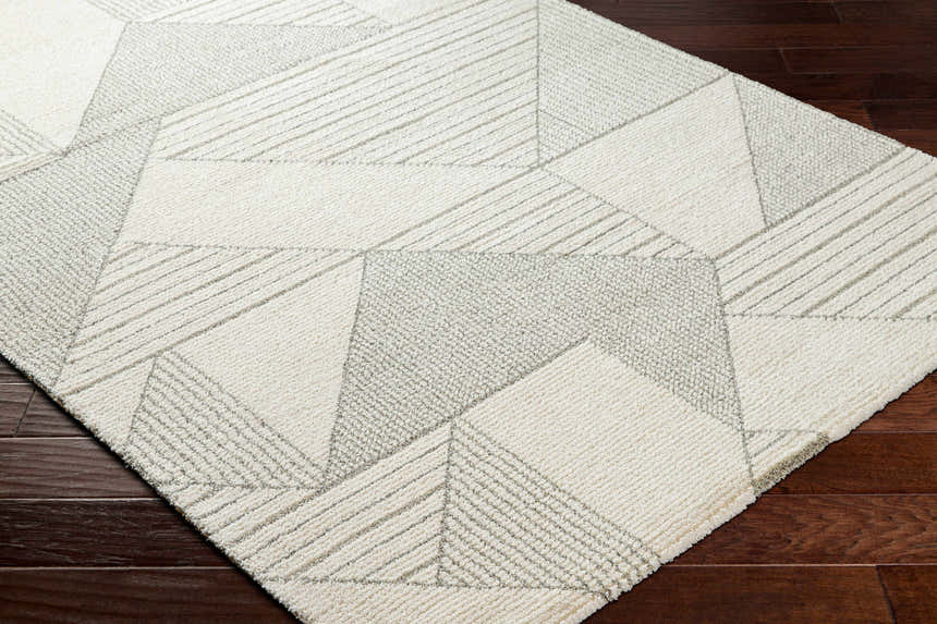 Close-up of the Wald Area Rug showing its beige and gray geometric pattern and textured weave on a dark wood floor. Corner