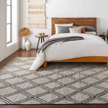 Bedroom scene with a Wausa Area Rug, featuring a black and cream geometric design, under a wooden bed frame. Roomscene-Rectangle