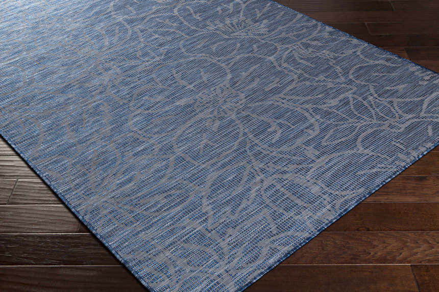 Close-up of blue Yackandandah Flatweave Area Carpet on dark wood floor. Floral pattern, machine woven texture. Clearance rug. Corner